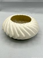 Ivory-toned ceramic squat bowl with ribbed spiral motif, visible curled rim detail, showing side angle view illustrating bowl depth and rib design.