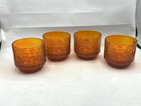 Four amber Tiki glasses showing the molded face design, arranged in a row.