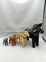 Four vintage hand-painted wooden Dala horses in varying sizes and colors lined up from smallest to largest.