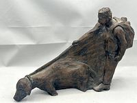 Front angle of stoneware sculpture showing figure with backpack holding leash from dog-like animal.