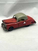 Side and front angled view of red tin crash car with beige hardtop roof showing details and condition.