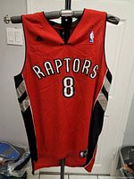 Full front view of the red Toronto Raptors jersey with black and silver side panels, number 8, and Raptors text.