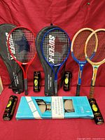 Lot overview showing 2 tennis rackets with cases, 2 wooden badminton rackets, 4 cans of tennis balls, and boxed badminton set.