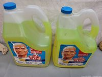 Two large plastic jugs of Mr. Clean disinfectant cleaner with blue caps and yellow-green contents, both labeled Summer Citrus and 5.2 L capacity.