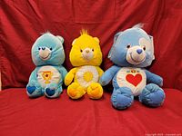 Three Care Bears plush toys sitting in a row against a red background.