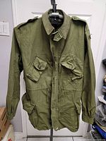 Front view of green Canadian Army combat jacket showing button flap pockets, collar, and sleeve patch.