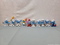 Wide shot showing all 10 Smurf figurines in a row, various poses and characters