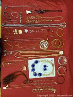 Full overview of costume jewelry laid out on a red cloth showing variety of necklaces, rings, earrings, bracelets, and brooches.