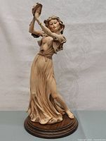 Full view of porcelain figurine depicting dancing woman playing tambourine on wooden base.