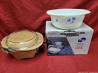 Three heat-resistant opal glassware casseroles: two amber-colored with lids and one white with blue flower design, displayed on a box labeled 'Heat-Resistant Opal Glassware RP'