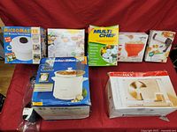 Overview of all kitchen appliances and accessories in their original boxes displayed on a red cloth background.