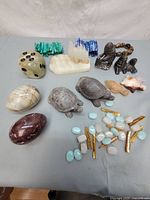 Full lot of natural stone items showing carved turtles, polished stones, figurines, and small stone beads and pieces on a gray cloth surface.