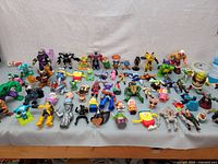 Wide shot of about 40 assorted superhero and character figurines in various styles laid out on a table.