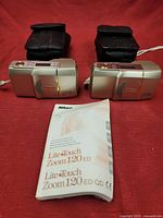 Two Nikon Lite Touch Zoom 120 ED AF 35mm film cameras placed side by side with black protective cases behind them and instruction manual in front.