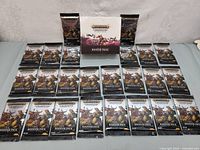 24 foil-sealed booster packs laid out in front of the sealed display box, all Warhammer Age of Sigmar Champions booster packs.