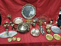 Full view of assorted precious metal items arranged on red cloth including trays, goblets, bowls, candle holders, and decorative pieces.