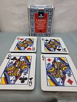 Front view of the set of four ceramic serving plates each featuring a different Queen playing card suit, displayed alongside the original box.