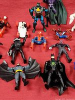 Top-down view of assorted superhero mini figures spread over a red surface. Includes eight figures with Batman, Spider-Man, and other characters.