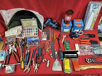 Overview of assorted hand tools and accessories including pliers, wrenches, screwdrivers, heat gun, lantern, and electric connector box on red background.