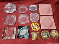 All items in the lot displayed on red cloth, showing variety of ashtrays in glass, ceramic, metal, and painted styles