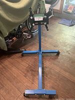 Blue metal engine stand with I-shaped base and caster wheels in garage setting.