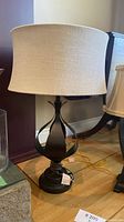 Full view of the lamp showing black metal base with twisting design and taupe fabric shade
