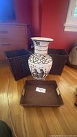 View of four items together: one large decorative vase and three large woven baskets, placed on wooden floor.