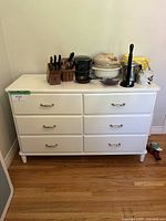 Front view of white 6-drawer dresser with household items on top.