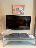 Front-facing photo showing the Sony TV mounted on the wall with the gray TV stand underneath, accessories visible on the stand