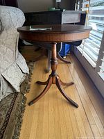 Side angle view of the antique Duncan Phyfe oval pedestal accent table next to a couch, showing the oval top and the turned pedestal base with four curved legs and brass capped feet.