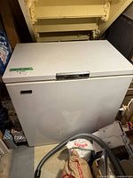Photo of white Beaumark chest freezer closed, positioned in basement under stairs, showing top and latch handle.