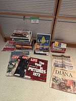 Wide view of all books, magazines, and newspapers included in the lot, arranged on floor showing variety of items and covers