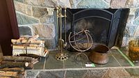 Overview of fireplace accessories arranged on hearth including copper pot, decorative metal orb, brass fire tool holder with tools, and black wrought iron screen.