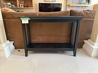 Front view of the espresso console table placed against a brown couch, showing the raised lip around the top shelf and lower shelf.