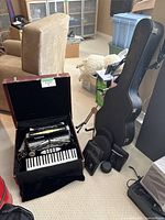 Wide shot showing accordion in open case, guitar stand, guitar case, and accessories