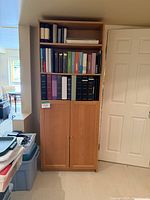 Front view of the tall wooden bookshelf filled with binders and books.