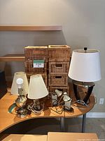 Photo showing four lamps on a wooden surface beside nine wicker baskets stacked and arranged in background.
