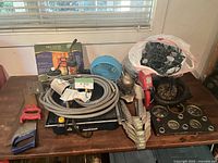 Overview photo showing Mastercraft tile saw, coiled hoses, propane torch, blue fan, metal gauges, and various tools on wooden table.