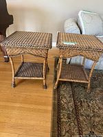 Two square rattan end tables positioned next to each other on a wood floor, showing woven tops and lower shelves.