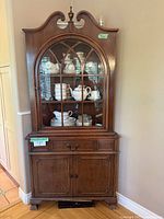 Straight-on view showing entire vintage solid wood curio cabinet in room corner with items displayed inside and storage below.