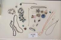 Overview photo showing all vintage brooches, necklaces, pins arranged on white surface.