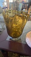Amber hand blown glass vase with wavy rim and thick clear base, placed on coffee table.
