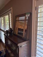 Vintage window mirror resting on furniture near window blinds reflecting the room interior