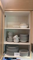 White dish set including plates, bowls, cups stacked in a kitchen cupboard.