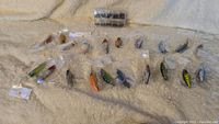 Overview of 20 fishing lures in original packaging and a box of fishing hooks laid out on a blanket.