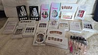 Overview shot of all 21 packages of unopened false nails and nail items arranged on a light fabric surface.