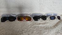 Eight pairs of Oakley sunglasses in a row showing different frame colors and lens types on a beige surface.