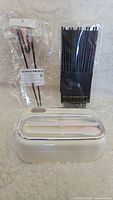 Photo showing white rectangular bento box with clear lid and beige tray, set of black chopsticks bundled in clear plastic packaging, and one pair of chopsticks separately packaged.