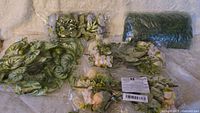 Various fake flowers, vines, and leaves laid out on a white textured surface, showing the packaging and assortment.