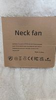 Brown cardboard box with 'Neck fan' text and product safety warnings, made in China.